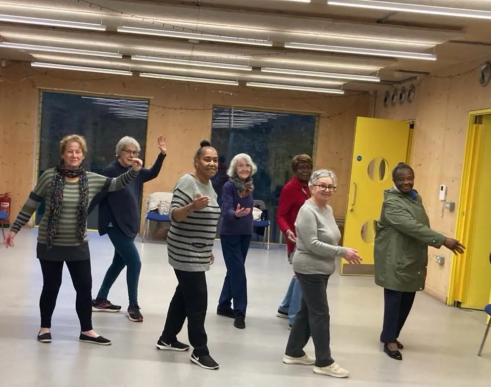 Seven members in a line rehearsing a dance step, smiling